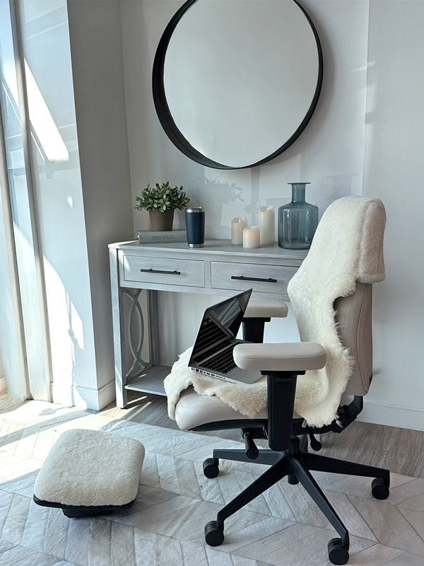 An open laptop rests on a white Lifeform Chairs office chair with a Hygge Cozy Shearling Cover in a sunlit home office.